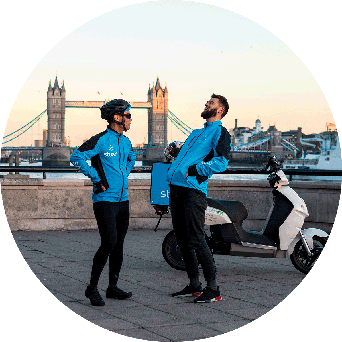 Two male Stuart couriers laughing, Tower Bridge in London is in the background. 