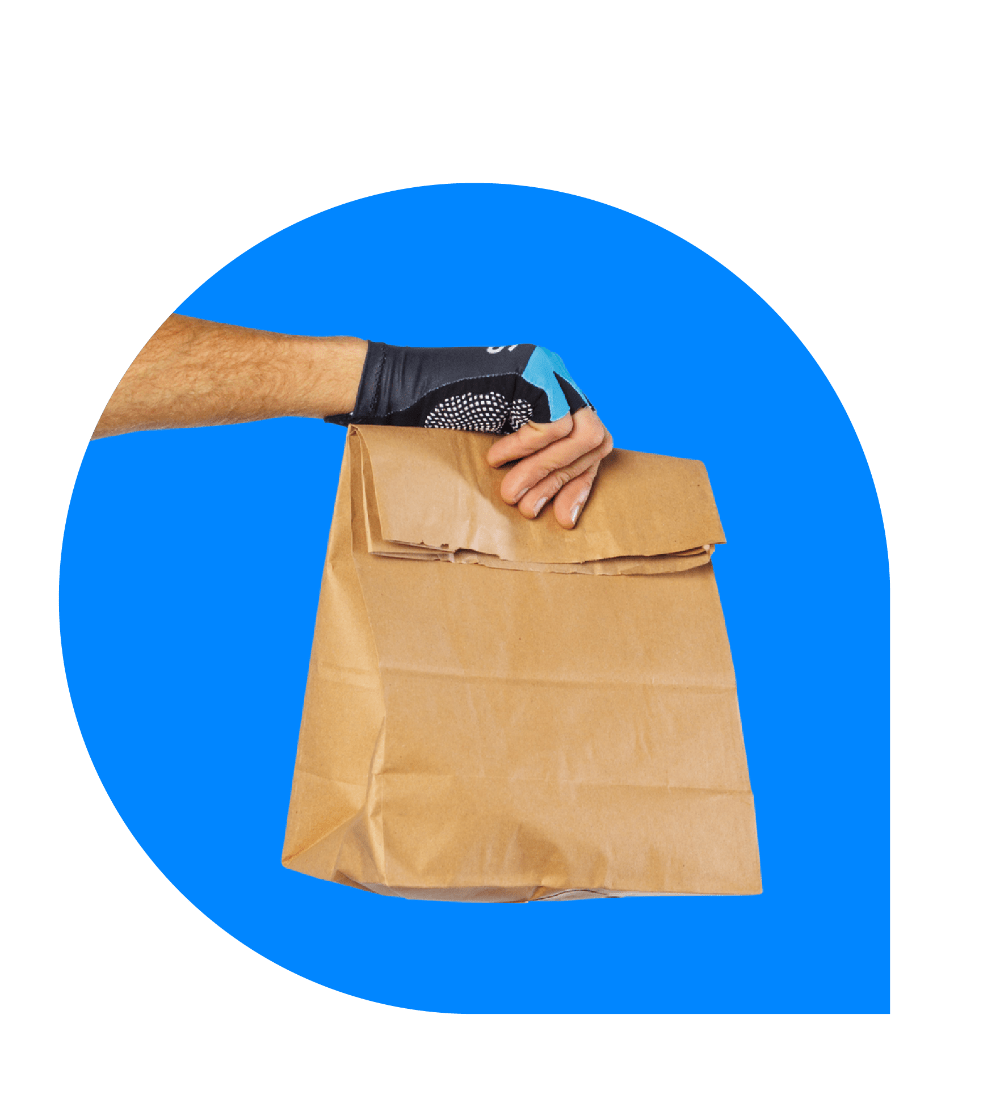 Main portant un gant marqué Stuart tenant un sac de livraison en papier kraft sur fond bleu