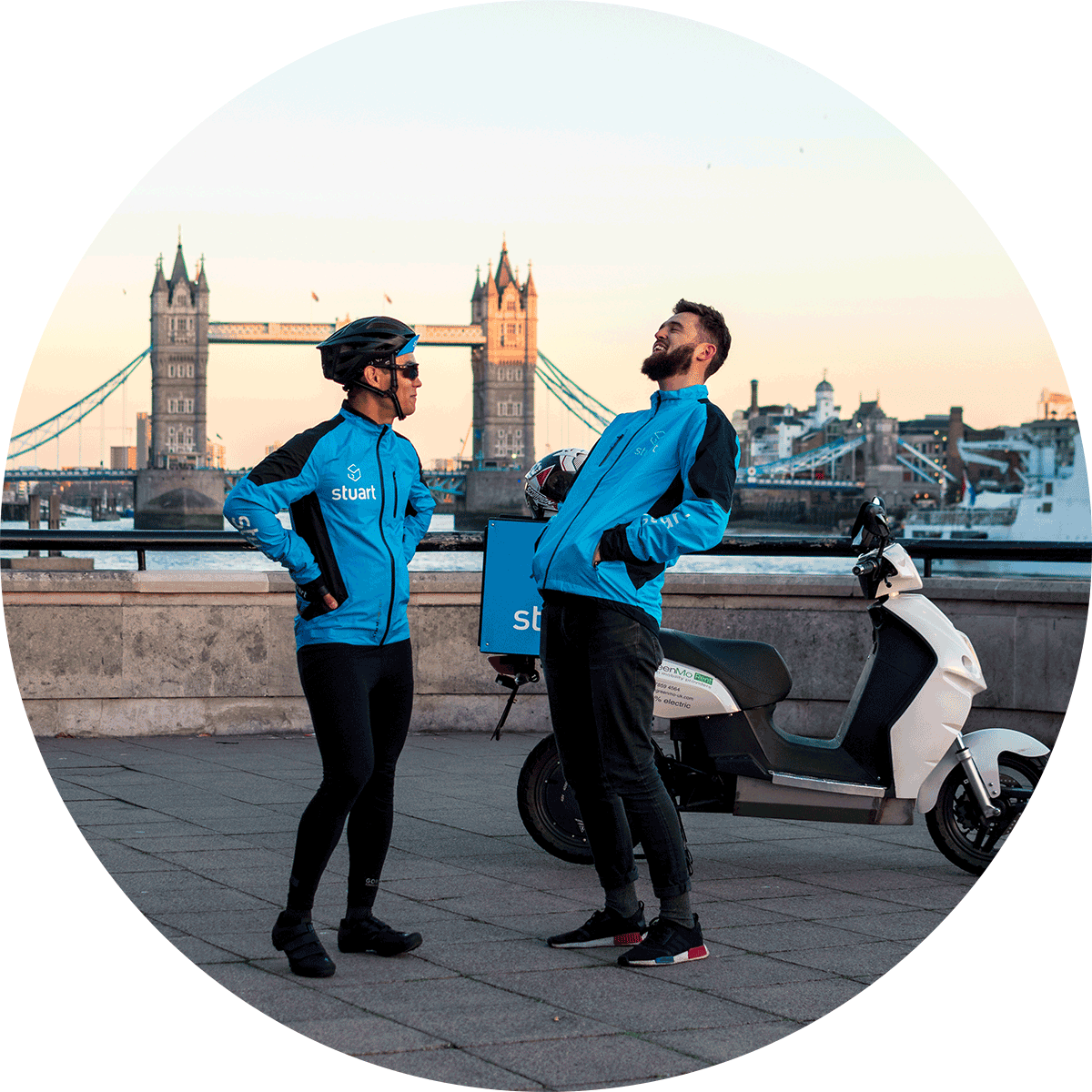 Two male Stuart couriers laughing, Tower Bridge in London is in the background. 